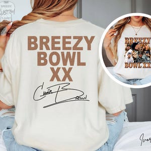 a person wearing a white t-shirt with the text "BREEZY BOWL XXX" printed on it, along with a signature. The person is also wearing a necklace and has their hair styled in braids.