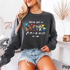 A woman wearing a gray sweatshirt with a graphic design of characters from the TV show "Friend in Me" and the text "You've got a FRIEND in ME" printed on it.