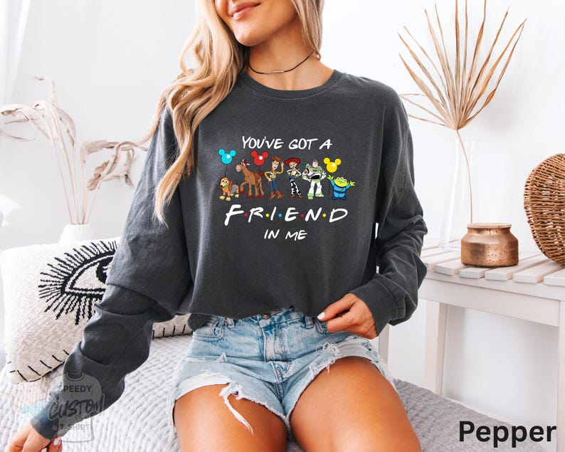 A woman wearing a gray sweatshirt with a graphic design of characters from the TV show "Friend in Me" and the text "You've got a FRIEND in ME" printed on it.