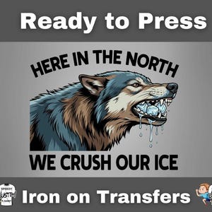 May include: Iron-on transfer featuring a wolf with ice cubes in its mouth, with the text "HERE IN THE NORTH WE CRUSH OUR ICE." The wolf is depicted in shades of blue, brown, and white against a gray background. The words "Ready to Press" and "Iron on Transfers" are also present.