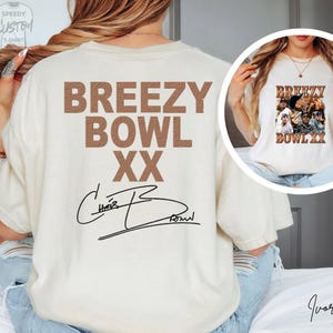 a person wearing a white t-shirt with the text "BREZY BOWL XX" printed on it.