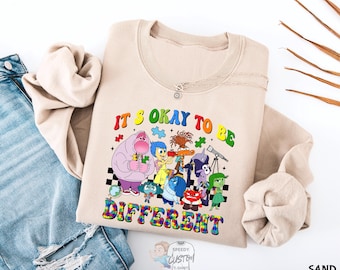 May include: A tan sweatshirt with a graphic print of characters from the movie Inside Out. The text on the shirt reads "It's okay to be different".