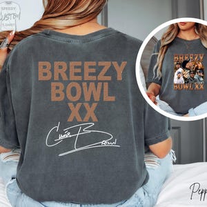 a person wearing a grey t-shirt with the text "BREEZY BOWL XX" printed on it.