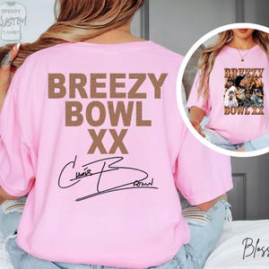 A woman wearing a pink t-shirt with the text "BREZZY BOWL XX" printed on it, along with a signature.