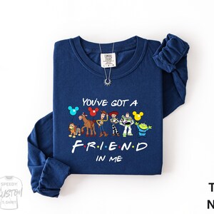 A navy blue long-sleeved t-shirt with a graphic design featuring characters from the TV show "Friends" and the text "You've Got a FRIEND in ME" printed on it.