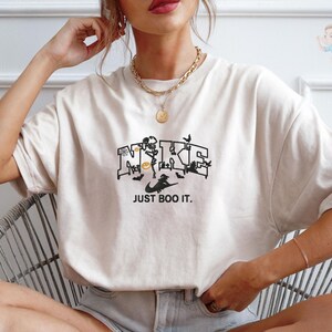 A woman wearing a white t-shirt with a graphic design and text, sitting in a chair.