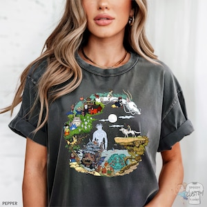 A woman wearing a gray t-shirt with a colorful, whimsical graphic design depicting various fantastical elements and characters.
