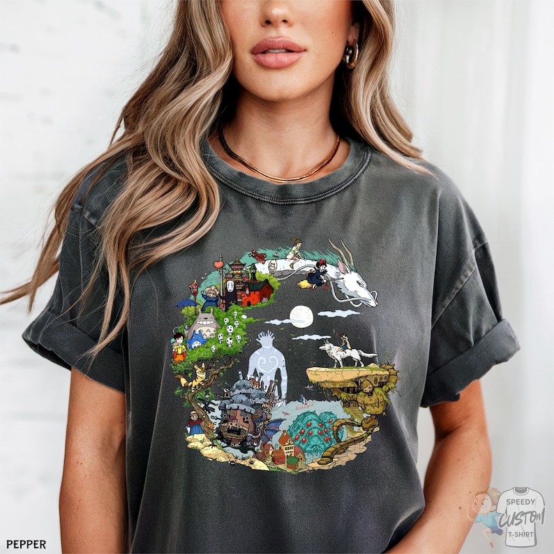 A woman wearing a gray t-shirt with a colorful, whimsical graphic design depicting various fantastical elements and characters.