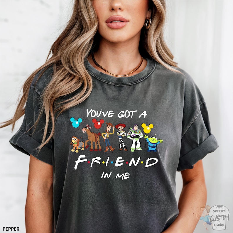 A woman wearing a gray t-shirt with a graphic design featuring characters from the TV show "Friends" and the text "You've Got a Friend in Me".