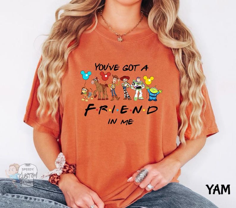 A person wearing an orange t-shirt with a graphic design featuring characters from the TV show "FRIEND IN ME" and the text "YOU'VE GOT A FRIEND IN ME".