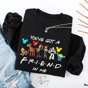 A black t-shirt with a graphic design featuring characters from the animated film Toy Story, along with the text "You've Got a Friend in Me" printed on it.