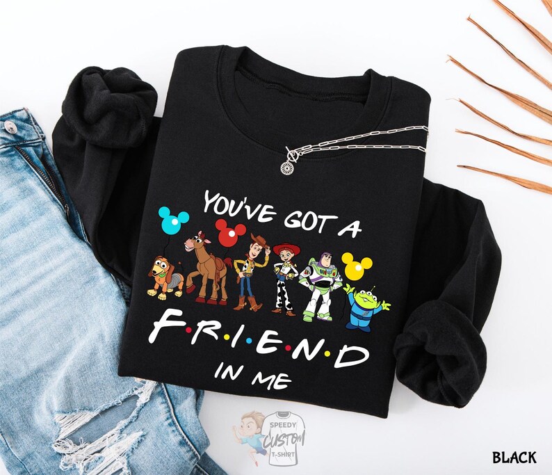 A black t-shirt with a graphic design featuring characters from the animated film Toy Story, along with the text "You've Got a Friend in Me" printed on it.