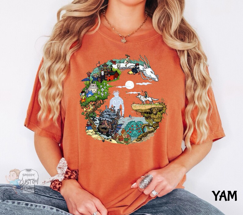A woman wearing an orange t-shirt with a colorful graphic design depicting various elements such as a castle, a dragon, and a moon.
