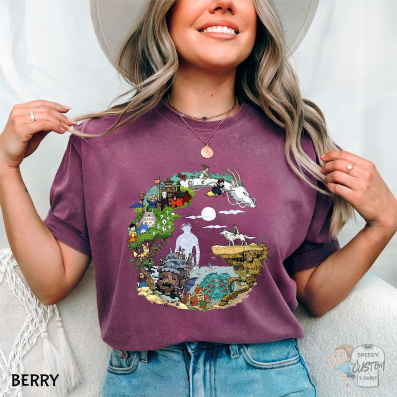 A smiling woman wearing a purple t-shirt with a colorful graphic design of a castle, a dragon, and a moon.