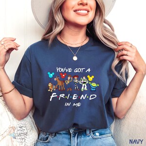 A woman wearing a navy blue t-shirt with a graphic design of various Disney characters and the text "You've Got a FRIEND in ME" printed on it.