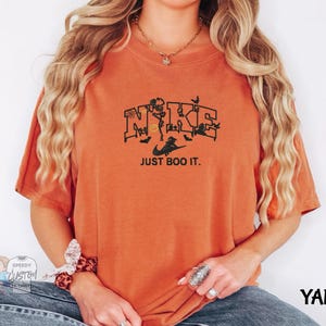 A woman wearing an orange t-shirt with a graphic design and text printed on it.