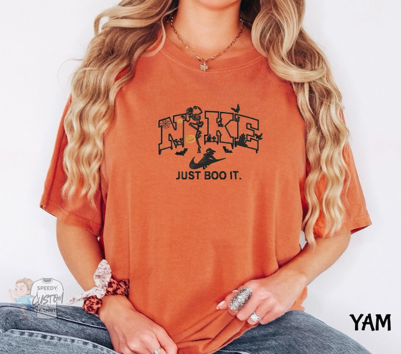 A woman wearing an orange t-shirt with a graphic design and text printed on it.