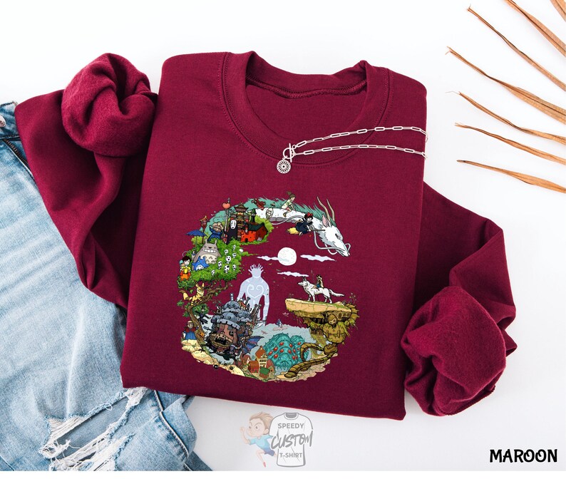 A maroon sweater with a colorful, illustrated design depicting various elements such as a castle, animals, and a moon.
