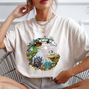 A woman wearing a white t-shirt with a colorful graphic design depicting a castle, a unicorn, and various other elements.