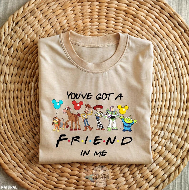A beige t-shirt with a graphic design featuring characters from the animated film Toy Story, along with the text "You've got a FRIEND in ME" printed on it.