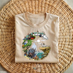A beige t-shirt with a colorful, illustrated collage design depicting various scenes and characters from the Studio Ghibli film "Spirited Away".