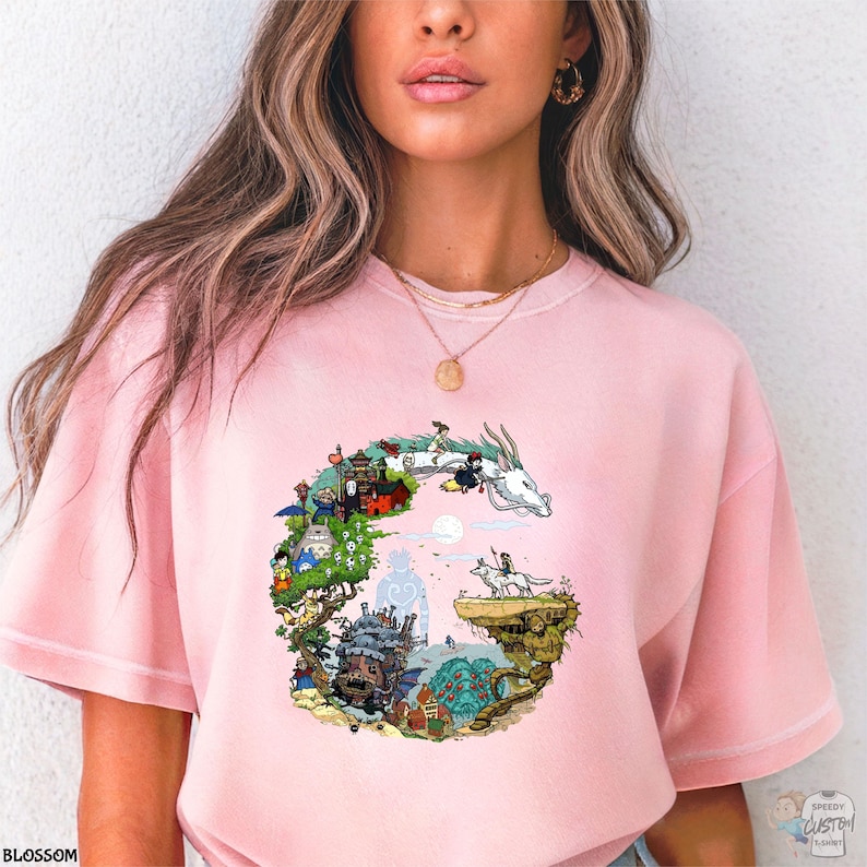 A woman wearing a pink t-shirt with a colorful, whimsical graphic design depicting a castle, a dragon, and various other fantastical elements.
