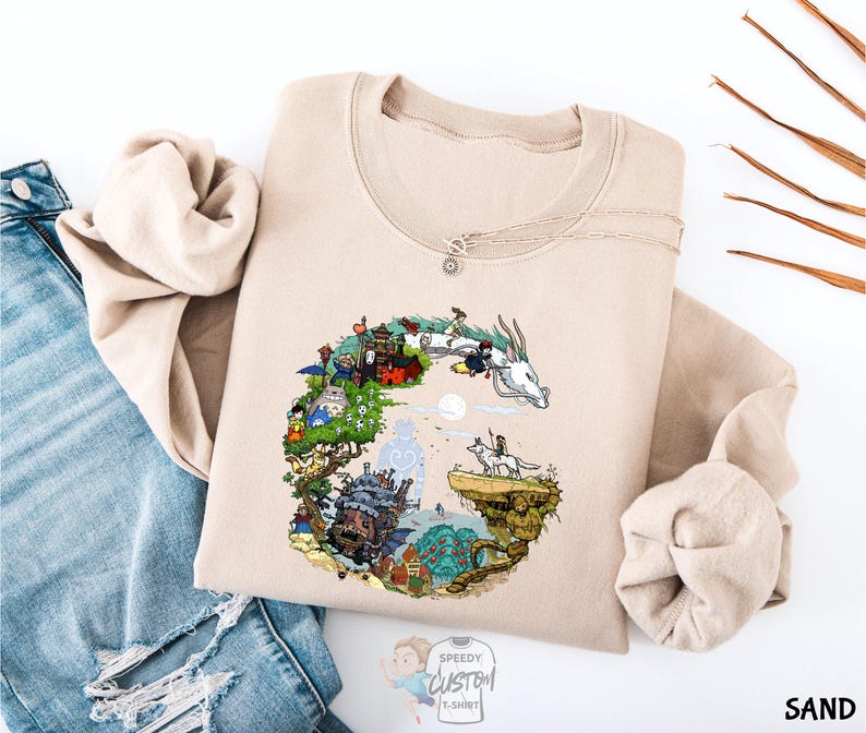 A beige sweatshirt with a colorful illustration of a dragon and various other elements, such as buildings, trees, and a castle, is displayed on a white background.
