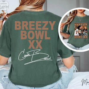 a person wearing a green t-shirt with the text "BREEZY BOWL XX" printed on it.