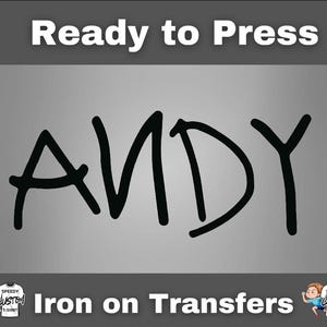 May include: Black iron-on transfer with the name "ANDY" in a bold, handwritten font. The text "Ready to Press" is above the name, and "Iron on Transfers" is below. The background is a gradient of gray.