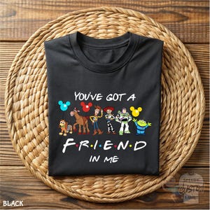 A black t-shirt with a graphic design featuring characters from the animated film Toy Story, along with the text "You've Got a FRIEND in ME" printed on it.