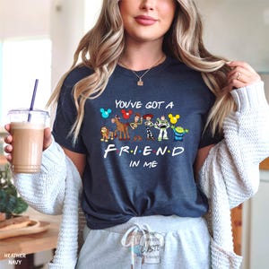 A woman wearing a blue t-shirt with a Disney character design and text, holding a drink in a plastic cup.