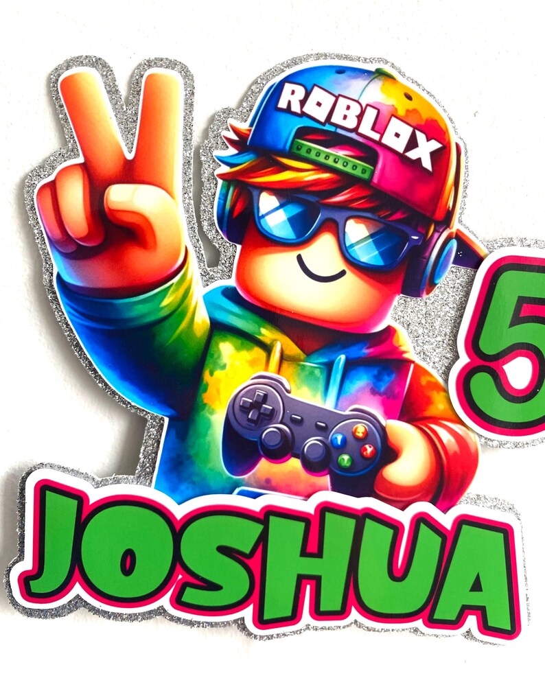 May include: A colourful cake topper featuring a Roblox character wearing a blue and red hat with the word "Roblox" on it. The character is holding a video game controller and has a green and pink name tag that says "Joshua".