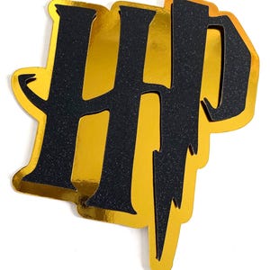 May include: A gold and black glittery HP logo, with a lightning bolt, on a white background. The letters are black with glitter, and the background is gold. The logo is likely for a Harry Potter theme.