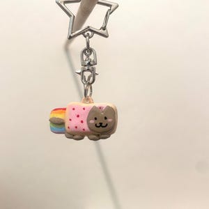 May include: A pink and brown cat-shaped keychain with a rainbow tail. The keychain is attached to a silver star-shaped key ring.
