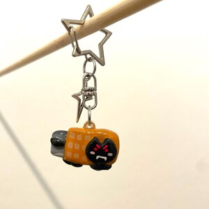 May include: A yellow and black cat-shaped keychain with a waffle pattern on its back. The keychain is attached to a silver star-shaped charm and a silver chain.