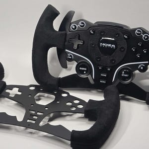 May include: Black racing wheel with a suede-like grip and a perforated metal frame. The wheel features multiple buttons, dials, and the "MOZA Racing" logo. The design suggests a focus on performance and control for sim racing.