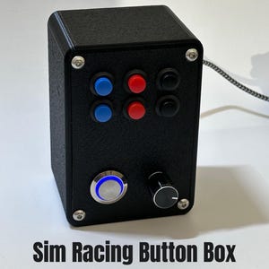 Könnte beinhalten: Schwarze Sim-Racing-Button-Box mit blauen, roten und schwarzen Knöpfen, einem Drehknopf und einem blau beleuchteten Knopf. Der Text "Sim Racing Button Box" wird unten angezeigt. Die Box ist mit silbernen Schrauben befestigt.