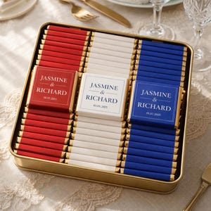May include: A gold rectangular box filled with chocolate bars in red, white, and blue, resembling a flag. Each chocolate bar is individually wrapped with gold foil. The labels read "Jasmine & Richard" with a date.