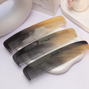 May include: Three horn combs with fine teeth, each showing a colour gradient from dark to light. The middle comb has the word "kasuko" in script, and the bottom comb has "Linda". These combs are designed for hair care.