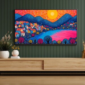 May include: A colorful landscape painting on a large TV screen. The artwork depicts a village with blue houses, mountains, and a vibrant pink and blue river under a bright yellow sun. The painting is framed in black and mounted on a wooden cabinet.