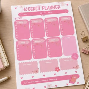 May include: A white weekly planner sheet with pink accents, featuring the text WEEKLY PLANNER at the top. The layout includes sections for each day of the week, a notes section, and boxes labeled DON'T FORGET, REMINDERS, and GRATEFUL FOR, with butterfly graphics.