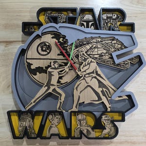 Könnte beinhalten: Ein mehrschichtiges Wandkunstwerk aus Holz zum Thema Star Wars. Das Design zeigt das Star Wars-Logo, Charaktere und Szenen, darunter Darth Vader und Luke Skywalker, die mit Lichtschwertern kämpfen. Das Stück ist in Grau, Gelb und Naturholztönen bemalt.
