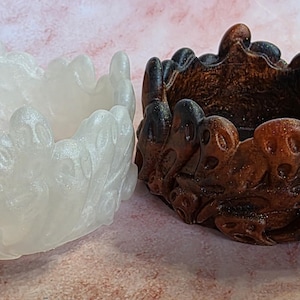 May include: Two decorative bowls. One is a pearlescent white, the other is brown with black accents. Both bowls have a unique, organic design with a textured surface. The bowls are likely for decorative purposes.