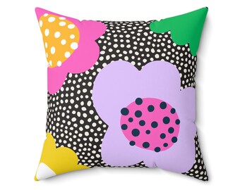 Könnte beinhalten: Quadratisches Zierkissen mit einem auffälligen Blumenmuster. Das Kissen zeigt große, stilisierte Blumen in Pink, Gelb und Lavendel vor einem schwarzen Hintergrund mit weißen Punkten. Ein grüner Akzent sorgt für einen Farbtupfer.