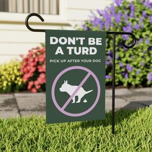 Könnte beinhalten: Eine dunkelgrüne Gartenflagge mit dem Text "DON'T BE A TURD PICK UP AFTER YOUR DOG" und einer weißen Hunde-Silhouette in einem rosa Kreis mit einem Querstrich. Die Flagge steht auf einem schwarzen Metallständer im Garten.