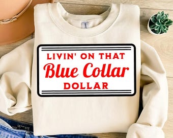 May include: Cream-colored sweatshirt with a black and white rectangular graphic. The graphic reads "LIVIN' ON THAT Blue Collar DOLLAR" in red and white text. A casual, everyday apparel item.