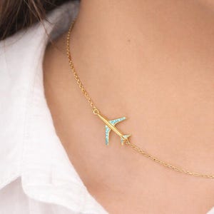 May include: A gold-colored airplane pendant necklace with turquoise accents. The necklace is worn on a person wearing a white shirt. The Etsy logo is visible in the bottom right corner.