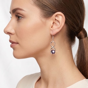 May include: A silver-toned earring featuring a twisted metal infinity-style frame that holds a single, round, dark purple bead at the base. The earring hangs from a simple hook wire, showcasing a polished metallic finish and a deep violet stone.
