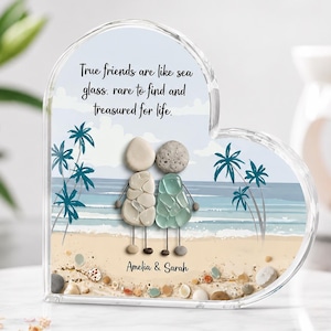 May include: A heart-shaped acrylic plaque featuring a beach scene with two figures crafted from pebbles and sea glass. The text reads: True friends are like sea glass, rare to find and treasured for life. Below the figures, the names Amelia & Sarah appear.