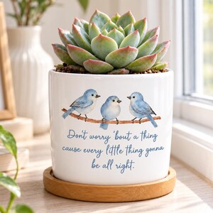 May include: A white ceramic planter with a wooden saucer containing a green succulent. The planter features a watercolor illustration of three blue birds on a branch and the text: Don't worry 'bout a thing cause every little thing gonna be all right.